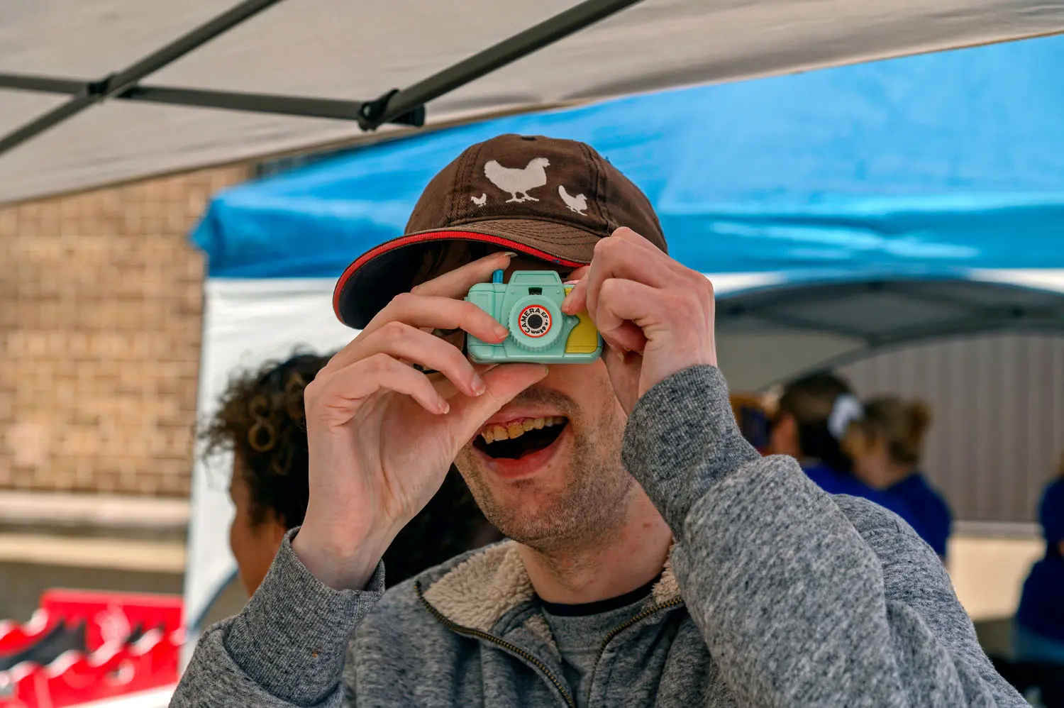Smiling person wearing a cap holds a small toy camera.