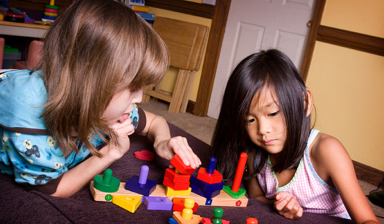 2 children around 7 years old, playing with blocks on a small table.