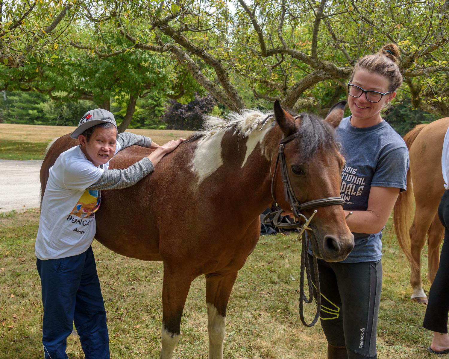 A man with a horse and the horse trainer. THe man is petting the horse, the horse trainer is holding on the reins and petting the horses nose area.