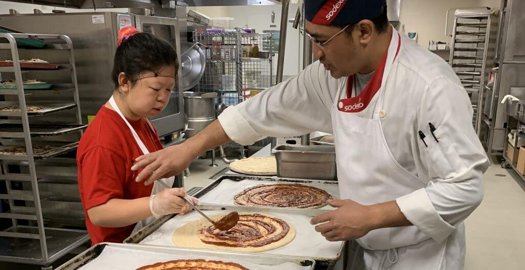 A chef and sous chef creating a pizza together in an industrial kitchen
