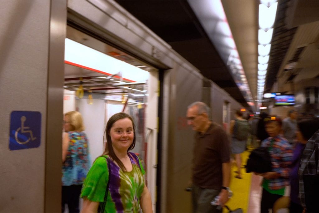 Jenna coming out of the TTC train with a smile. Wearing a green, purple and yellow tie-dye T-Shirt.