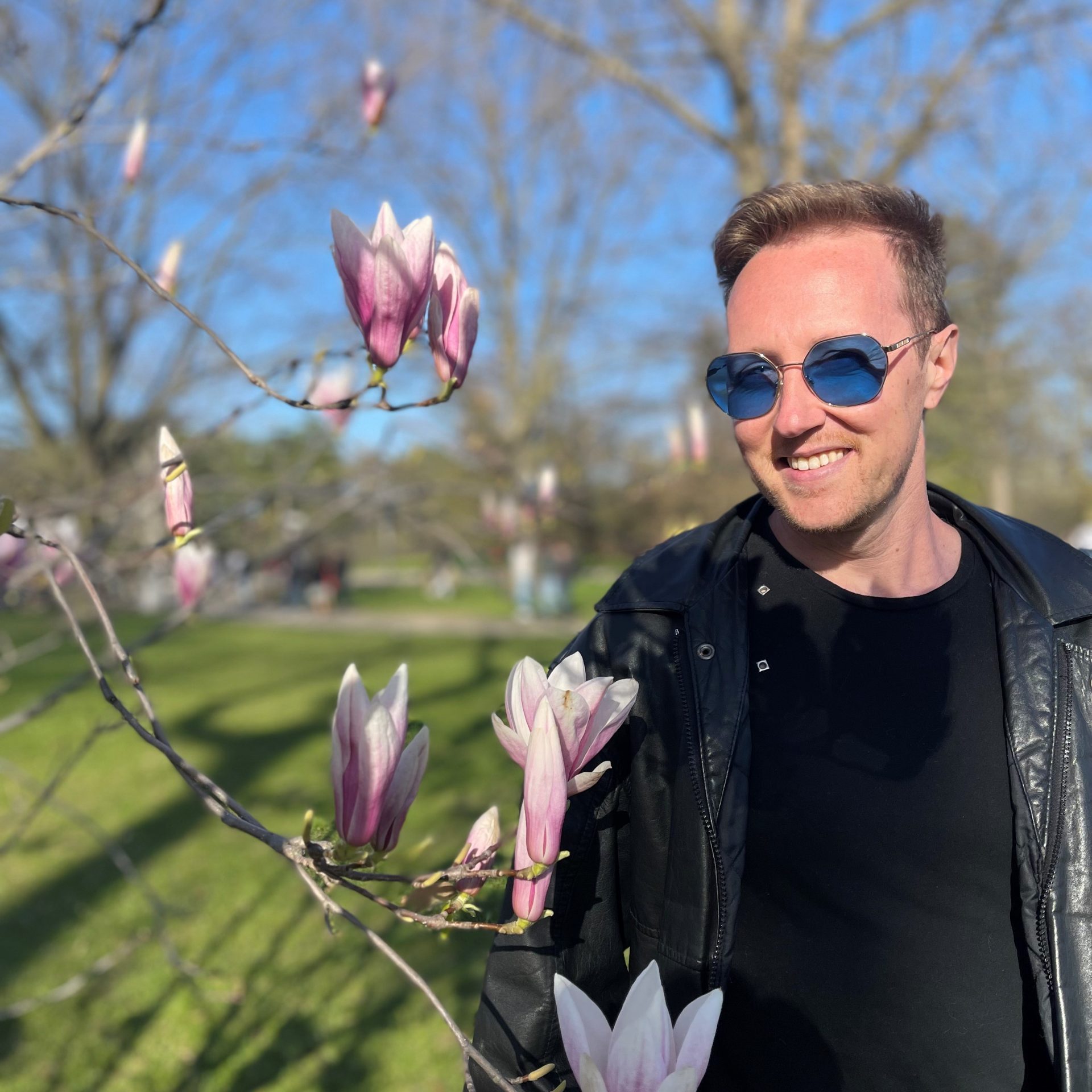 Derek, wearing blue lensed sunglasses posing with a branch of Cherry Blossoms.