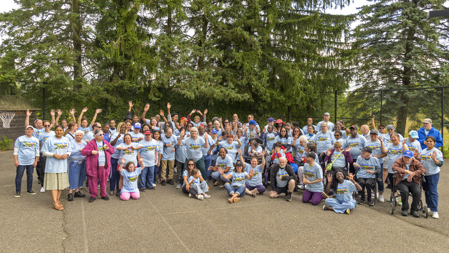 Huge group photo with all guests of Farm day. Wearing the same blue t-shirt and everyones hands are up with smiles on their faces