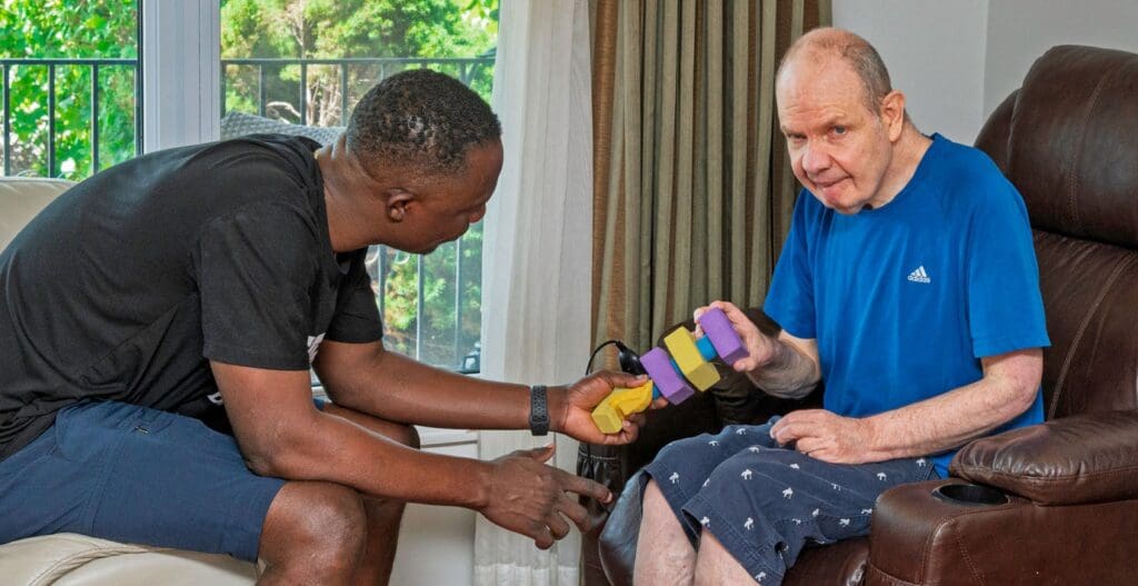 2 men sitting on opposite chairs facing each other. Both are holding a sensory toy together,