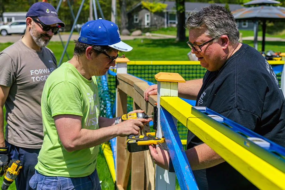 Three people working together on an outdoor building project, using tools and teamwork to complete a community improvement activity.