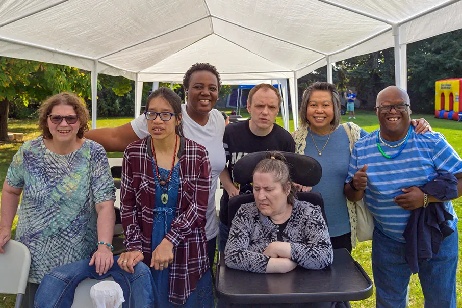 Group of community members gathered under a tent at an outdoor event, smiling together and celebrating connection and inclusion