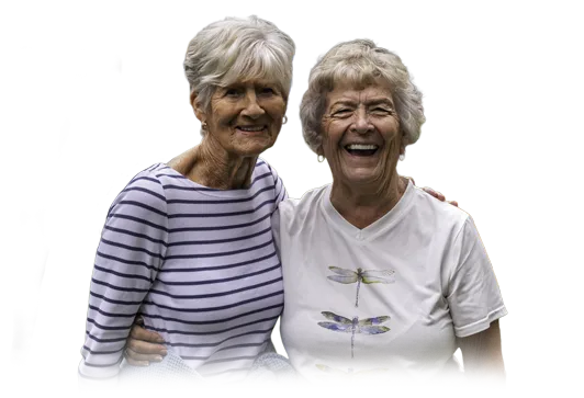 Two smiling older women, a family member and caregiver, with their arms around each other