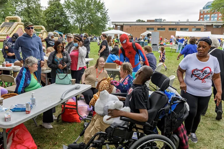 Large group of people gather outdoors at a community event, with games, tables, and costumes.
