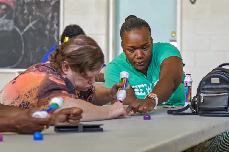 Two people work together at a table during a creative activity, using colourful markers and craft materials.