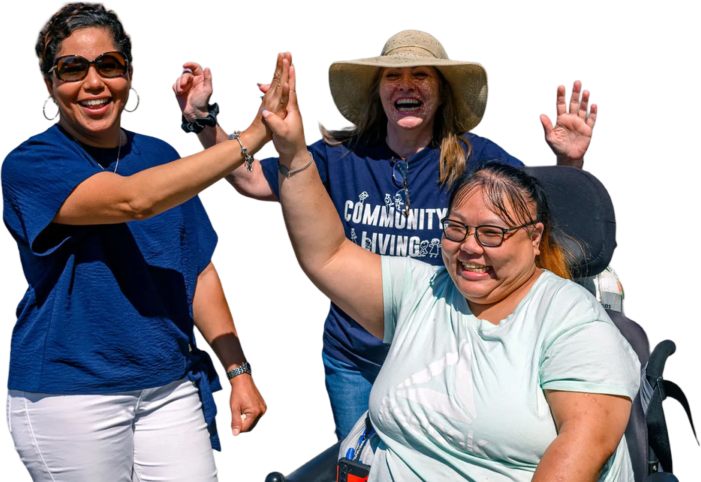 Three people smiling and high-fiving outdoors at a Community Living event, including tenants and community members in the background.