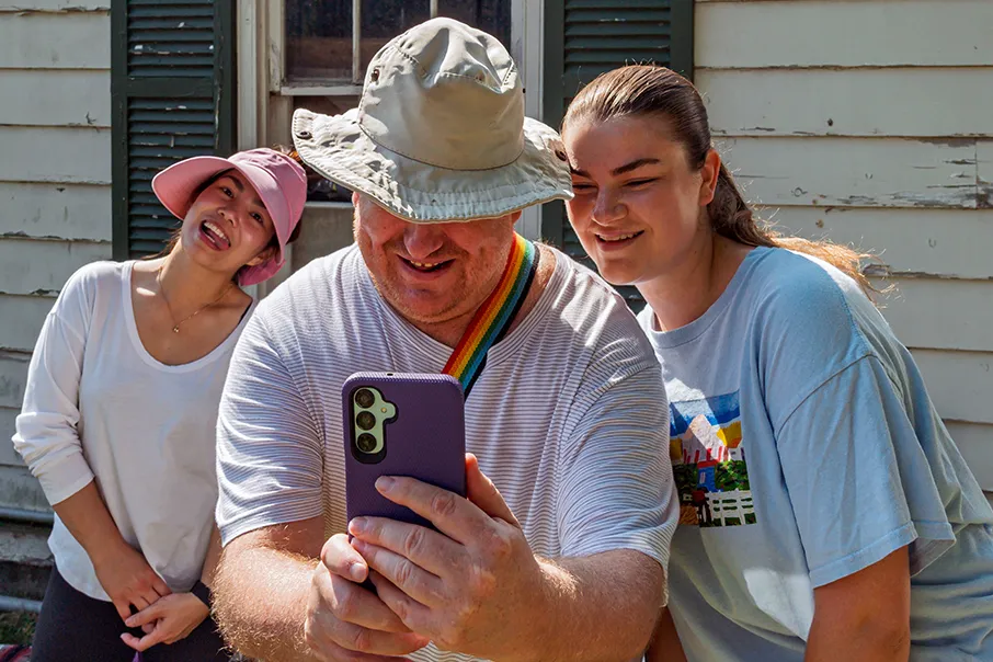 Three people smiling together while taking a selfie outdoors on a sunny day.