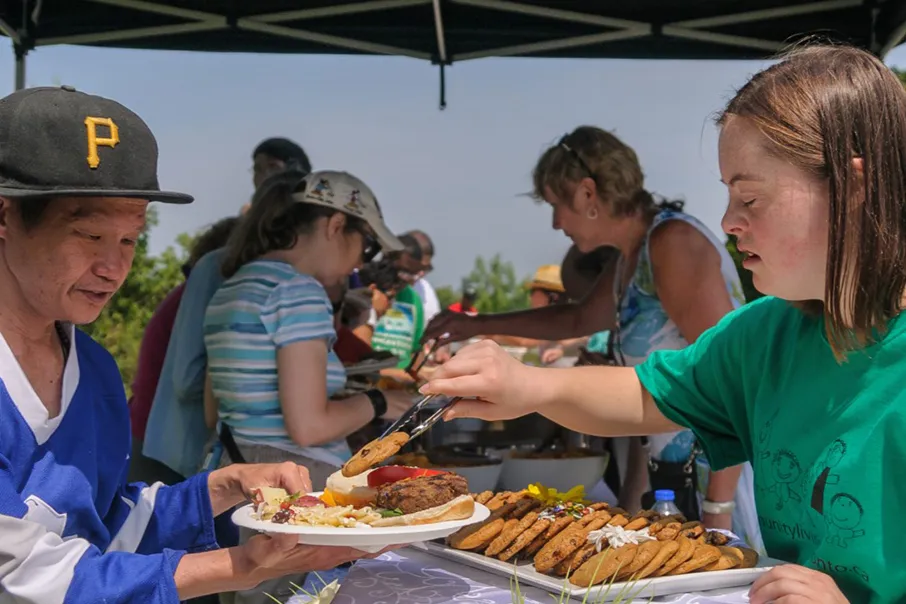 People enjoying a community barbecue together, serving food, sharing a meal, and connecting in an inclusive outdoor gathering.