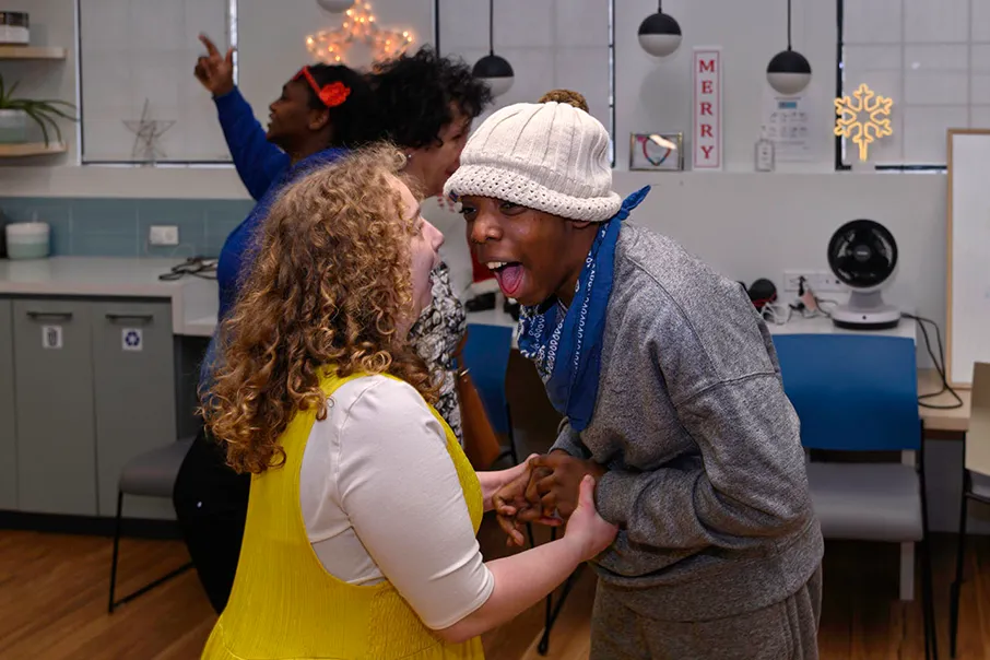 Two people sharing a joyful moment together, holding hands, laughing, and connecting in a welcoming and inclusive community space.