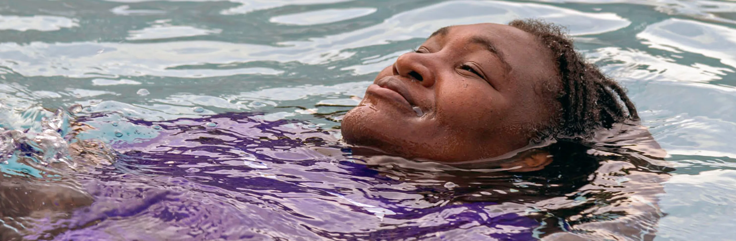 A person floating peacefully in a swimming pool, smiling with eyes closed while relaxing in the water.