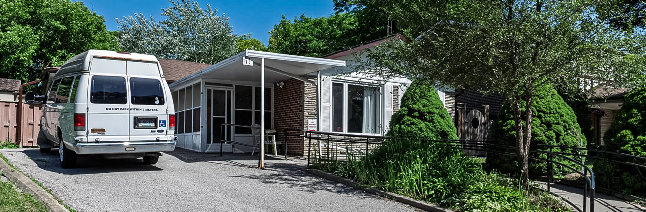An accessible home with wheelchair ramp and parked accessible van in a quiet residential neighbourhood on a sunny day.