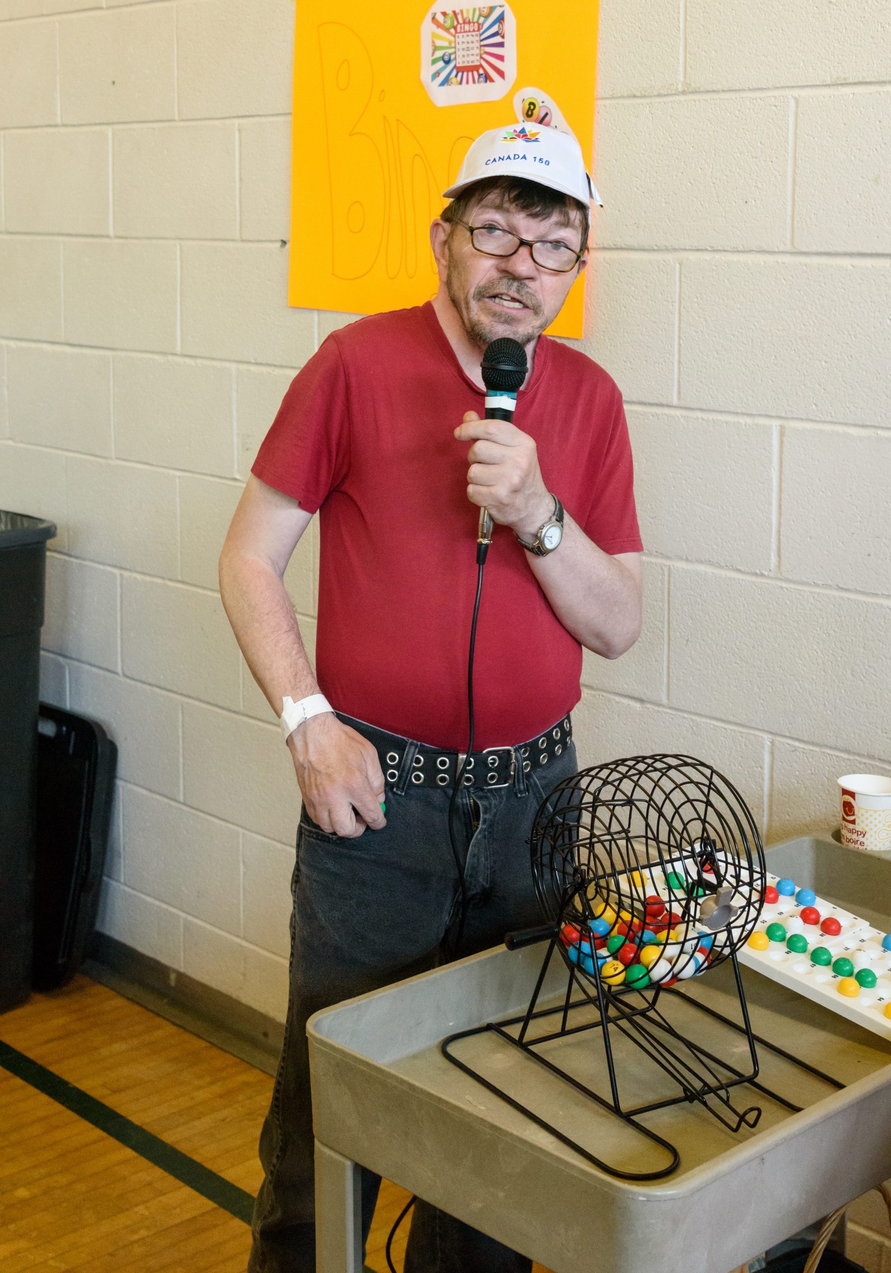 The announcer of a bingo game. Holding a microphone standing behind the BINGO numbers draw.