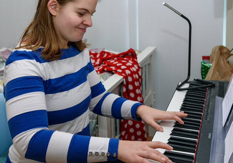 A woman wearing a blue and white striped shirt, playing a piano